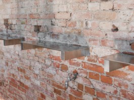 Development and production of three stainless steel tables with an integrated fireplace and rotatable arms with hooks to hang cheese over heat, a glass vitrine and small storage spaces by ErtlundZull. Development and production of three wall mounted stainless steel shelves and a four-legged roof by ErtlundZull, Gerswalde 2021. Concept by Argument GmbH. Photos by Studio Bowie. ErtlundZull