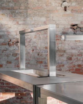 Development and production of three stainless steel tables with an integrated fireplace and rotatable arms with hooks to hang cheese over heat, a glass vitrine and small storage spaces by ErtlundZull. Development and production of three wall mounted stainless steel shelves and a four-legged roof by ErtlundZull, Gerswalde 2021. Concept by Argument GmbH. Photos by Studio Bowie. ErtlundZull