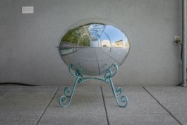 A mirrored roundshaped sculpture standing on ornamental legs in an outside area. ErtlundZull