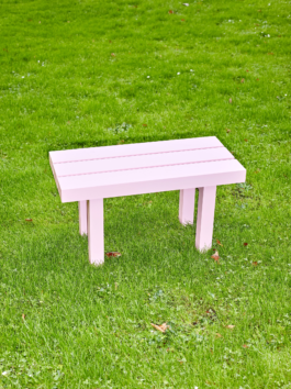 Small light pink aluminium bench from the furniture series Pretending It's Wood. Placed on bright green grass. Designed by ErtlundZull. Photographed by Robert Hamacher. ErtlundZull