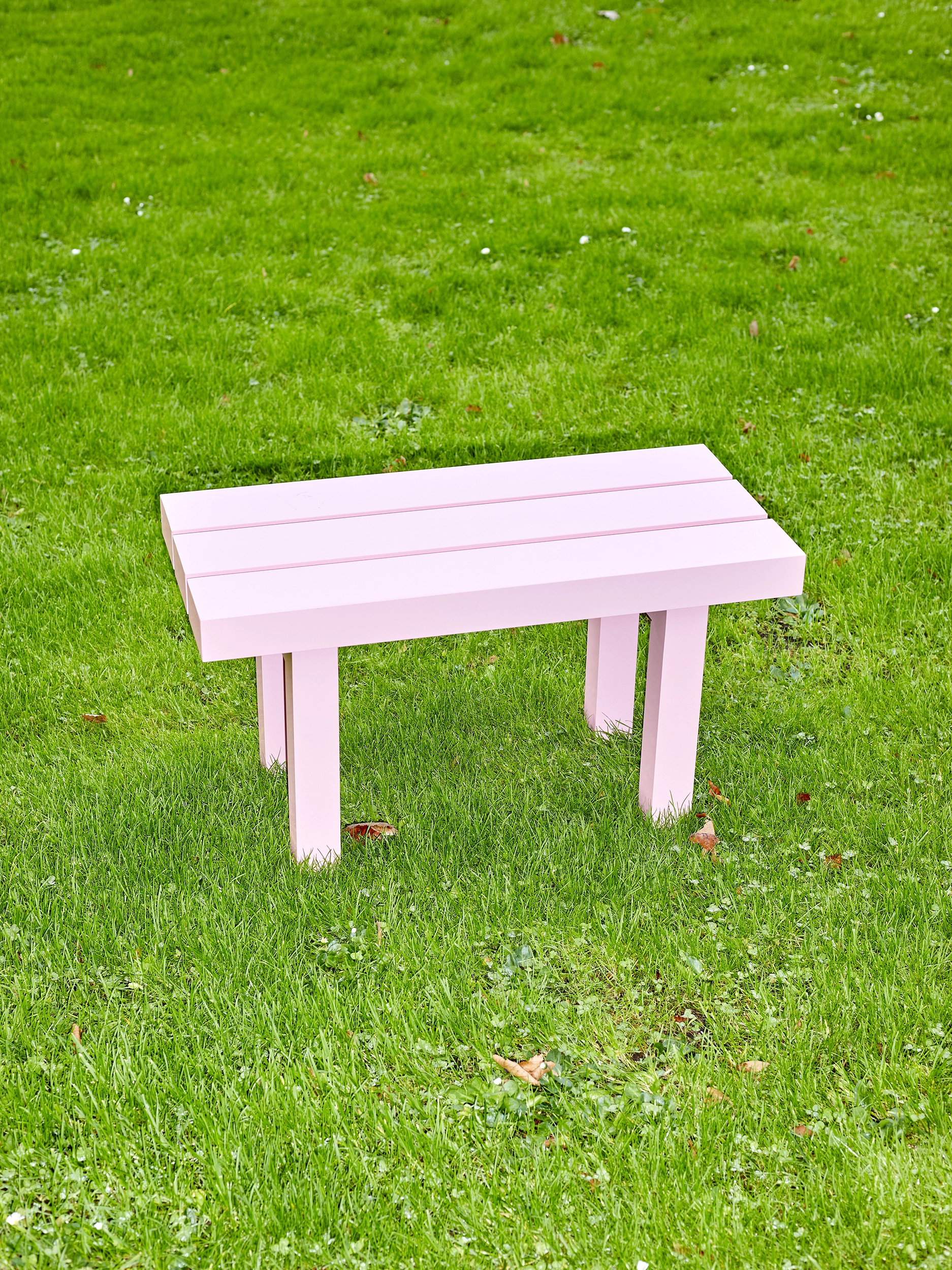 Small light pink aluminium bench from the furniture series Pretending It's Wood. Placed on bright green grass. Designed by ErtlundZull. Photographed by Robert Hamacher. ErtlundZull