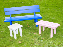 Seating group of the aluminium furniture series Pretending It's Wood placed outside on bright green grass. Big blue bench with backrest in the center, white stool in the front left, small light pink bench on the right. Designed by ErtlundZull. Photographed by Robert Hamacher. ErtlundZull